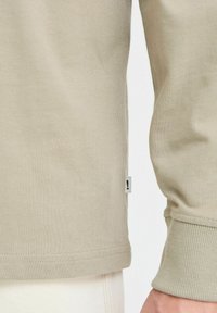 Katoenen longsleeve shirt in lichtbeige met ribgebreide boorden en zoom; heeft een klein merkembleem aan de zijnaad.