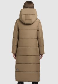 Dlhý, polstrovaný hnedý kabát s kapucňou, s vodorovným prešívaním, vo voľnom strihu a logom na dolnom ľavom okraji. Hladká textúra.