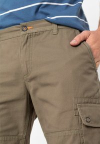 Pantaloni cargo khaki con chiusura a bottone, tasche laterali con patta e un tessuto liscio e resistente con dettagli di cucitura visibili.