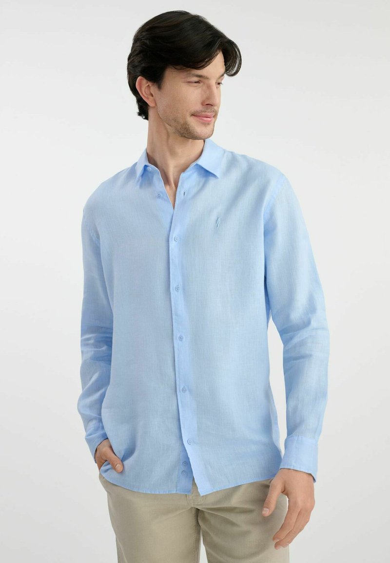 Jasnoniebieska, długa koszula z fasonem button-up, uszyta z miękkiego, lekkiego materiału o subtelnej teksturze; posiada klasyczny kołnierzyk oraz mały detal z logo.