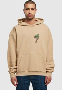 Beige hettegenser laget av mykt stoff, med en frontlomme og et lite grafikk av et palmetre og flamingo på brystet. Avslappet passform.