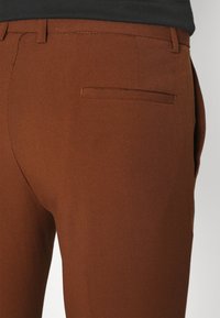 Brązowe spodnie dopasowane, charakteryzujące się gładką fakturą, slim fit oraz jedną tylną kieszenią w minimalistycznym stylu.