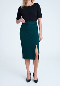Musta lyhythihainen toppi yhdistettynä polvipituiseen teal-väriseen kynähameeseen, jossa on sivuaukko ja pyöreä vyö. Asusteena mustat kärkitossut.