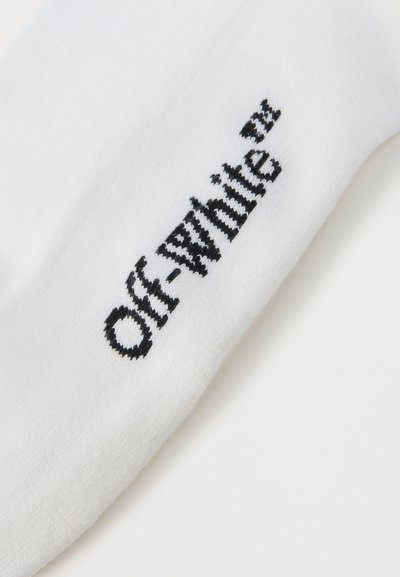 Λεπτομέρεια λευκού υφάσματος με μαύρο κεντητό λογότυπο "Off-White™" τοποθετημένο διαγώνια στην επιφάνεια.