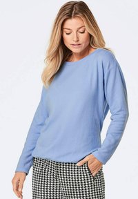 Hellblaues Fleece-Sweatshirt mit Rundhalsausschnitt, langen Ärmeln und lockerer Passform, kombiniert mit schwarz-weißen Hahnentritt-Musterhosen.