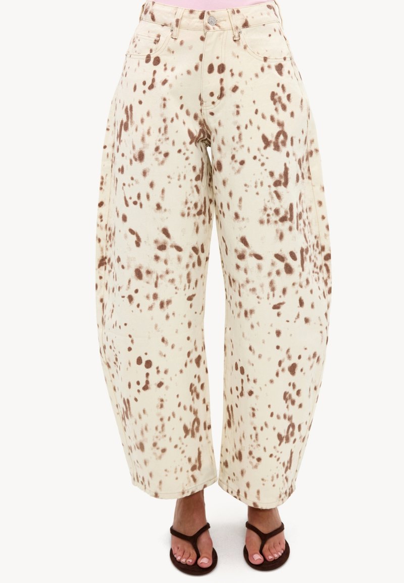Pantalon taille haute à jambes larges avec base crème et taches brunes irrégulières, porté avec des sandales noires fines.