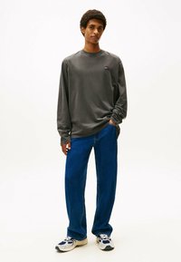 Camisa gris de manga larga, jeans azul de corte holgado y zapatillas blancas con detalles en azul marino. Diseño sencillo, ajuste casual. Sin patrones prominentes.