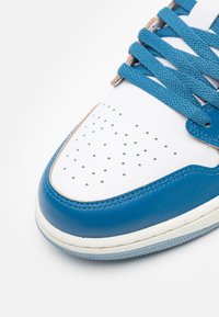 Gros plan sur la partie avant d'une basket blanche et bleue avec des lacets bleus et un embout en cuir blanc perforé.