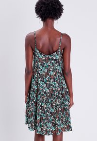 Robe à imprimé floral avec fines bretelles, présentant un fond noir avec des feuilles vertes et marron, offrant une silhouette fluide et une coupe ample.