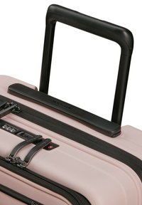 Hard-shell suitcase in soft pink with black accents, featuring a retractable black handle, dual zippers, and a built-in combination lock.
