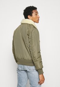 Olivgrüne Bomberjacke mit einem cremefarbenen Kunstfellkragen, elastischen Bündchen, geripptem Saum und gerafften Details an den Ärmeln.