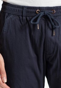 Pantalones azul marino de tela suave con cinturilla elástica, cordón ajustable y bolsillos laterales, con detalles de costura mínimos.