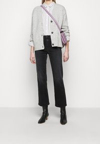 Cardigan en maille gris avec boutons, chemise rayée blanche et grise, jean court taille haute noir, et bottines noires. Sac à bandoulière violet.