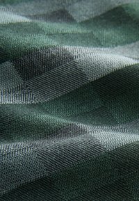 Tekstiili, jossa on vihreä ja harmaa houndstooth-kuvio. Materiaalissa on tekstuurimainen pinta, joka on pehmeä ja kudottu.