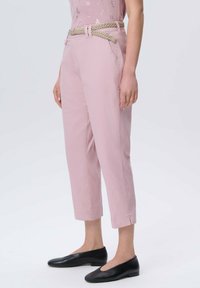 Jasnoróżowe spodnie z plecionym zielonym paskiem, ściętej długości, z przednimi kieszeniami i gładką teksturą. Połączone z czarnymi butami wsuwanymi.