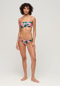 Set di bikini con base rosa, stampa a foglie in verde e arancione, spalline sottili e vita bassa. Texture liscia, colori vivaci.