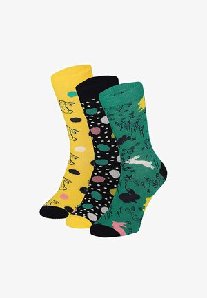 Drei bunte Socken mit unterschiedlichen Mustern: gelb mit Hasen, schwarz mit mehrfarbigen Punkten und grün mit Hasen und Ostereiern.