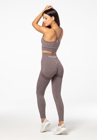 Sostén deportivo marrón y leggings de cintura alta hechos de una tela texturizada y elástica. Cuenta con tirantes finos y detalles de logo en la cinturilla.