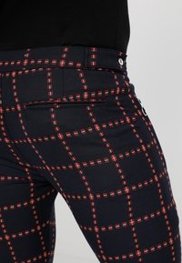 Marineblauwe broek met een rood-wit ruitpatroon, voorzien van een achterzakdetail en een slank, op maat gemaakt figuur.