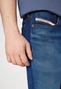 Jeans de denim azul oscuro con un ajuste slim, que presentan costuras en contraste, una etiqueta sutil en el bolsillo y una textura suave.