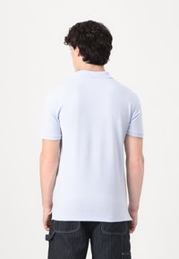 Světle modré polo triko s krátkými rukávy a klasickým límcem, vyrobené z hladkého materiálu, z pohledu zezadu. Žádné viditelné vzory nebo loga.