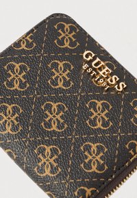 Juoda piniginė su reljefine danga, kurioje kartojasi auksinis logotipo raštas, ir auksinės spalvos detales. Uždarymas su užtrauktuku ir siuvinėtais akcentais.