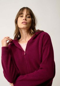 Burgundy huppari vetoketjulla, jossa on teksturoitu ribbikangas, hupullinen ja rento hihainen, päällä vaalea vaaleanpunainen paita.