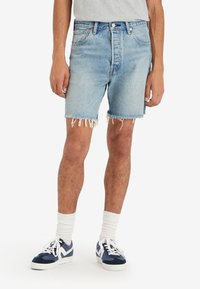 Pantalones cortos de mezclilla en un azul claro con un dobladillo deshilachado, diseño de tiro alto y estilo de cinco bolsillos, combinados con zapatillas de tenis en color navy y calcetines blancos.