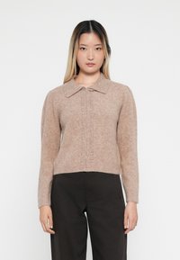 Lysebrun strikket cardigan med kragehals, med knappeåpning og dekorative perler langs fronten. Lange ermer og cropped passform.