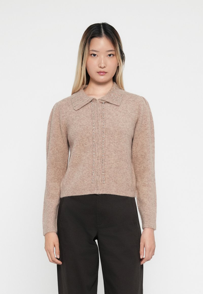 Lysebrun strikket cardigan med kragehals, med knappeåpning og dekorative perler langs fronten. Lange ermer og cropped passform.
