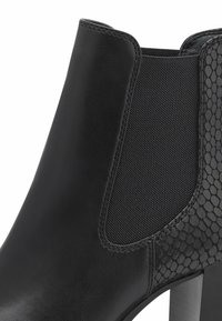 Černé kotníkové boty s hladkým koženým svrškem, elastickým panelem a texturovaným hadím vzorem. Obsahují robustní podpatek a prošité detaily.