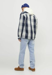 Giacca a quadri in navy e grigio con cappuccio bianco, abbinata a jeans azzurri e scarpe in suede marroni, vista da dietro.
