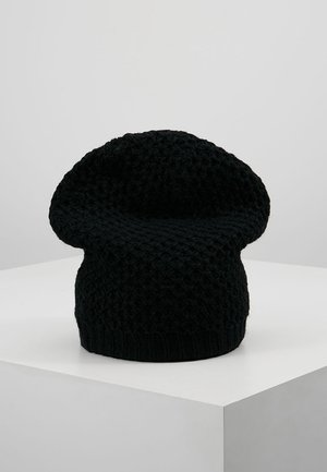 Béret tricoté noir avec motif losange texturé, présenté sur un socle blanc sur un fond gris clair uni.