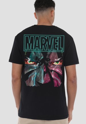 Mann trägt schwarzes T-Shirt mit neongrünem "MARVEL" Text und Grafik stilisierter intensiver Augen und metallischem Gesicht mit Blitzeffekten auf dem Rücken.