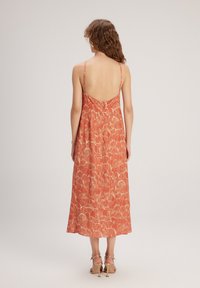 Maxikleid in Orange mit weißem Blättermuster. Verfügt über dünne Träger und einen niedrigen Rücken. Lockeres, fließendes Material mit einer glatten Textur.