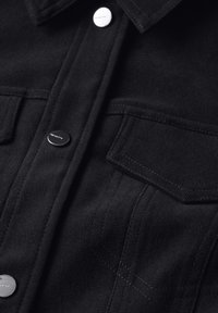 Svart denimskjorta med kragdetalj, två bröstfickor, silverfärgade tryckknappar och synliga sömnadsdetaljer på tyget.