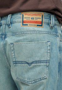 Ανοιχτό μπλε τζιν παντελόνι με δερμάτινη ετικέτα που γράφει "Diesel Industry", διαθέτει πίσω τσέπη με διπλές ραφές.