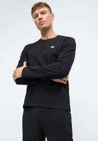 Musthave musta pika varrukas T-särk, mis on valmistatud siledast puuvillast, ümarate krae ja väikese valge logoga rinnal, koos mustade pükstega.