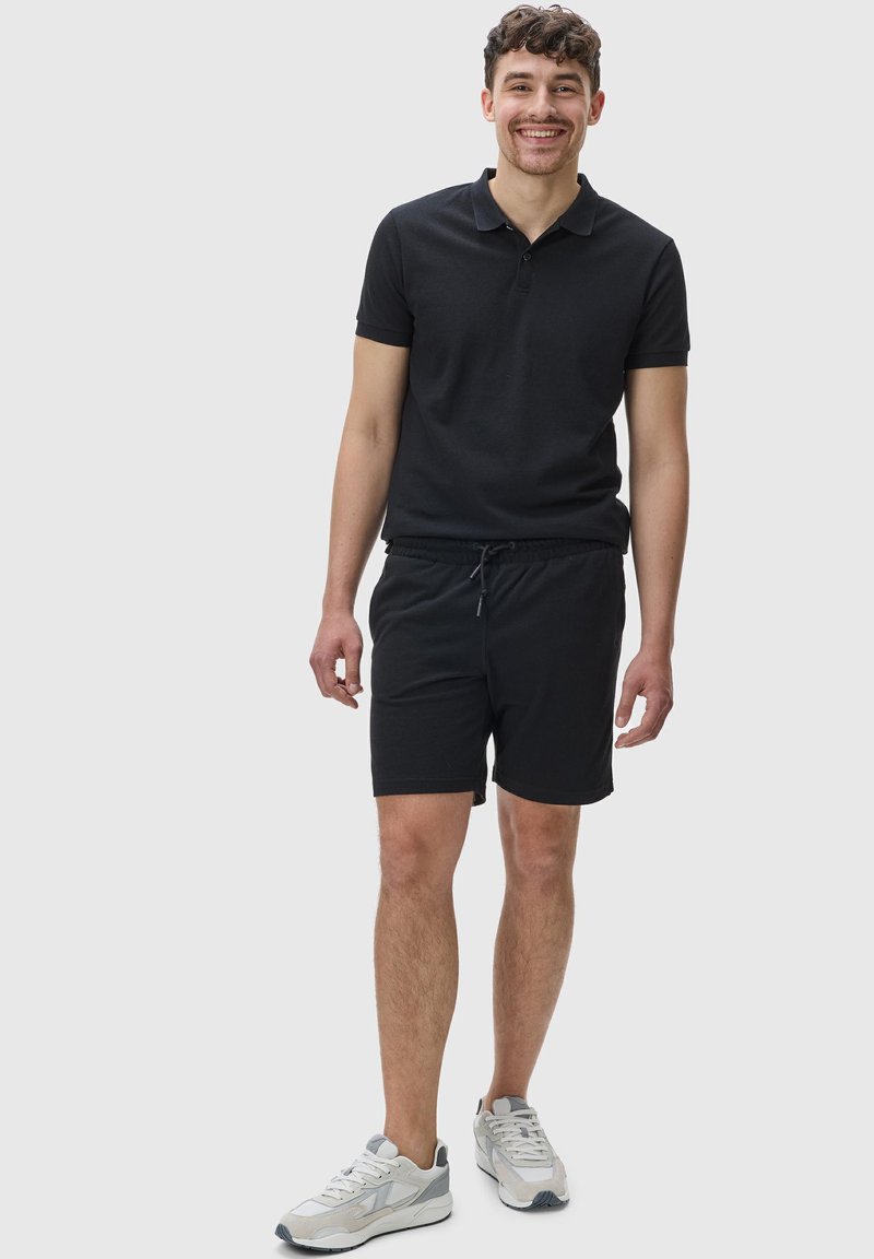 Černá polo triko s krátkými rukávy, spárované s elastickým pasem černými šortkami a světle šedými sportovními botami. Pohodlná tkanina ze směsi bavlny.