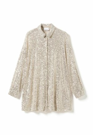 Beige sädelev särk pikkade varrukatega, terava kraega ja sirge lõikega. Omab säravat pinda, millel on vertikaalne mustriga detail.