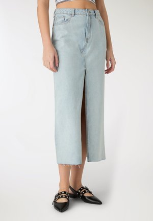 Gonna midi di denim azzurro chiaro con spacco frontale, orlo grezzo e design a cinque tasche, abbinata a scarpe slingback nere in vernice.