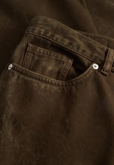 Pantaloni maro din catifea côtelată, cu un buzunar frontal prevăzut cu un nasture argintiu. Țesătura are un model texturat cu dungi și un aspect ușor uzat.