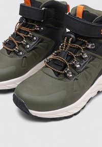 Bottes de randonnée en matériaux vert foncé et noir, avec sangle de cheville réglable, accents orange, œillets en métal et semelle texturée.