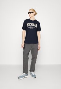Camiseta navy con gráfico de "MICHIGAN" en color crema, combinada con pantalones cargo grises. Calzado: zapatillas deportivas azul claro con acentos blancos.
