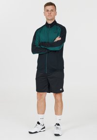 Svart och teal sportjacka med dragkedja framtill, som matchas med svarta shorts. Bärs med vita strumpor och svarta skor med en logotyp.