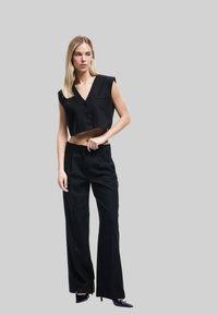 Zwarte cropped top met een V-hals en drie knopen, gecombineerd met hoge zwarte broeken met rechte pijpen en zijzakken.