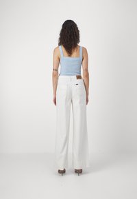 Débardeur à rayures bleu clair avec des bretelles ajustées, associé à un jean large blanc taille haute avec une étiquette de marque en cuir brun et des poches arrière.