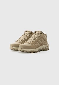 Chaussures de randonnée beiges en mélange de matériaux synthétiques texturés et de daim, offrant un bon maintien de la cheville, avec une semelle robuste pour la stabilité et l'adhérence.