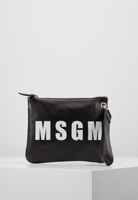 Pochette en cuir noir avec un logo MSGM blanc audacieux et une fermeture éclair, reposant sur une surface blanche contre un fond uni.