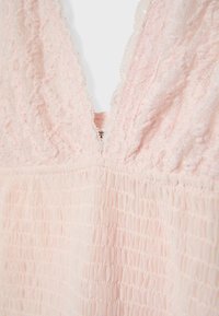 Light pink lace fabric with deep V neckline and ruched texture below the bust on a soft, delicate garment.